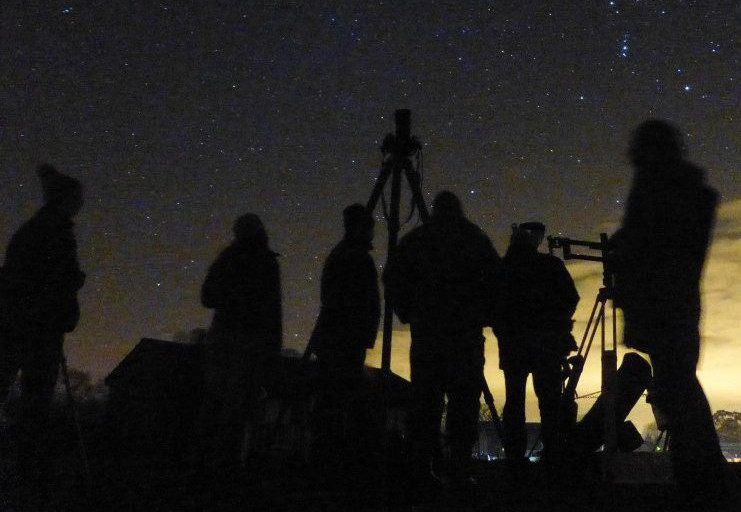 People standing with Telescopes at night.